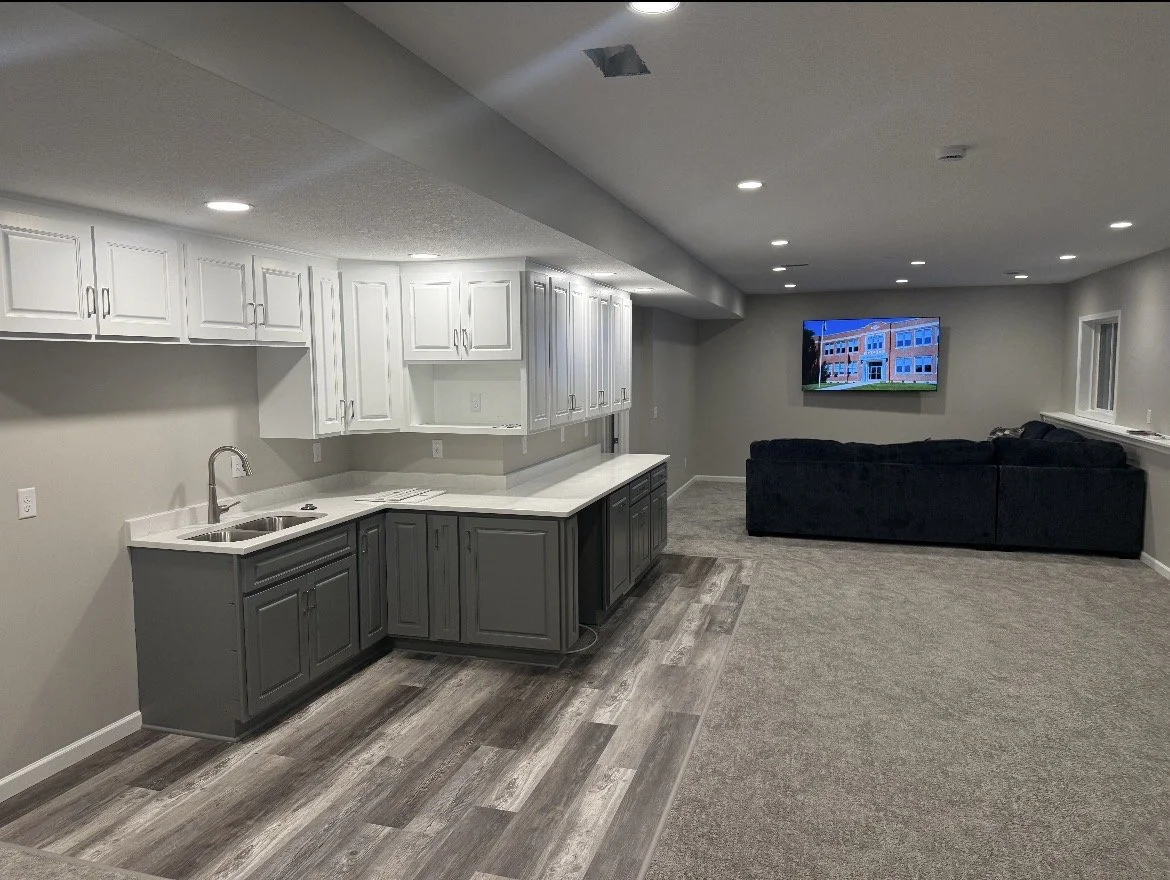 The same basement finished with a smooth drywall ceiling, recessed lighting, cabinetry, and flooring