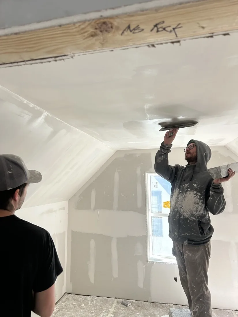 A Schroeder's Expert Wall pro skim-coating a vaulted ceiling while a homeowner watches and learns the technique