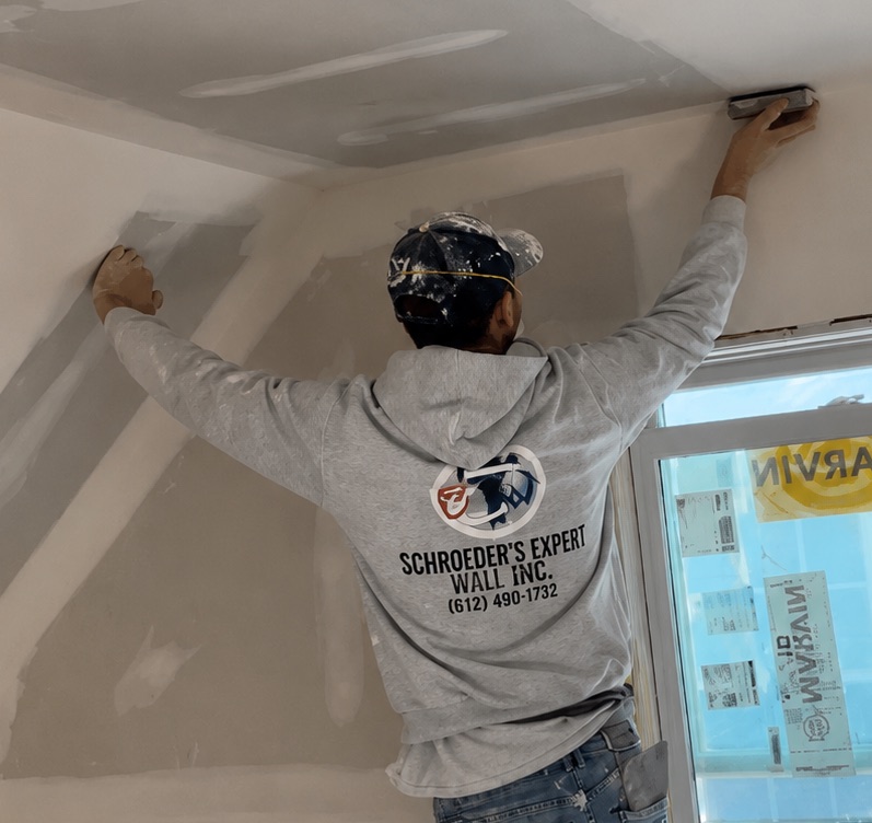 A painter finishing the wall-and-ceiling line near the corner of a room